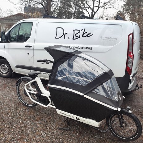 Vit van med Dr.Bike-logga. Det står även "di portabla cykelverkstad". Framför bilen syns en vit cykel med plastkapell